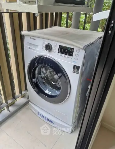 Modern Samsung washing machine on a balcony with a view of greenery.
