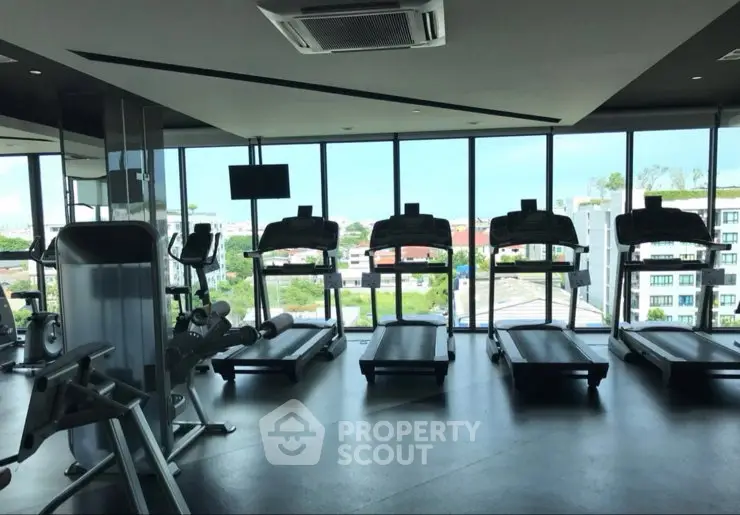 Modern gym with treadmills and panoramic city view in luxury apartment building.