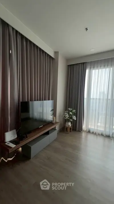 Modern living room with large windows and stylish curtains, featuring a sleek TV setup and elegant flooring.