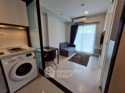 Modern compact living room with integrated kitchen and washing machine, featuring sleek furniture and natural light.