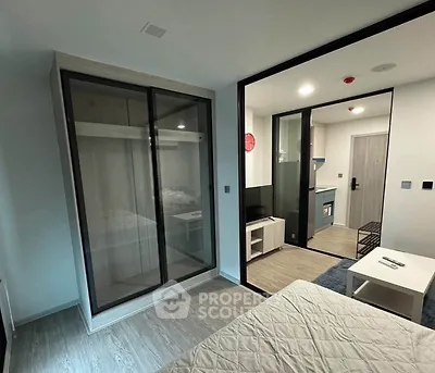 Modern studio apartment with sleek glass wardrobe and compact kitchen area.