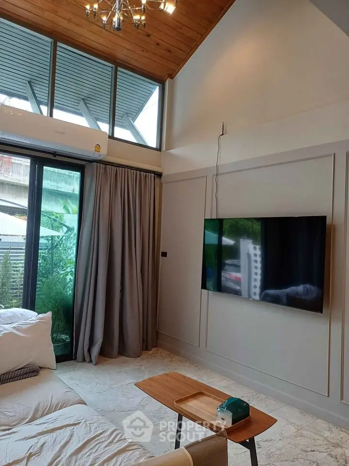 Modern living room with high ceiling and large windows, featuring a wall-mounted TV and stylish decor.