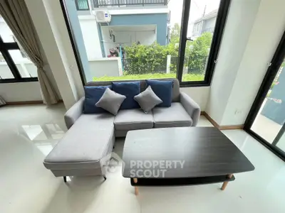 Modern living room with stylish sofa and coffee table, large windows offering garden view.
