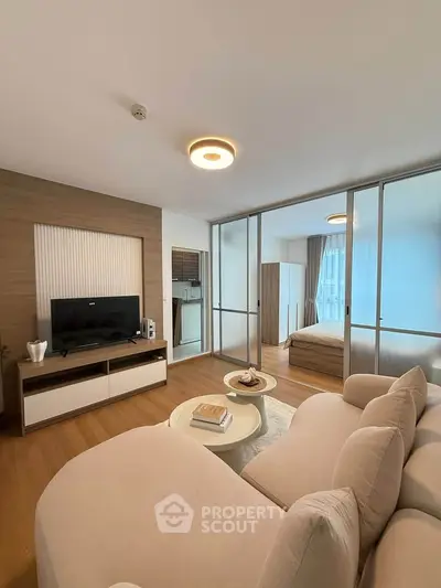 Modern living room with cozy seating and TV, adjacent to a stylish bedroom.
