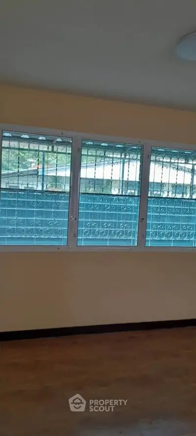 Spacious room with large windows and secure metal grilles, offering ample natural light and safety.