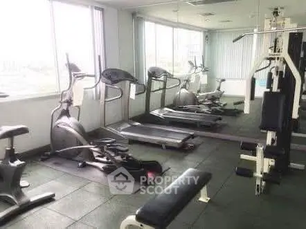 Spacious gym with modern fitness equipment and large windows offering natural light.