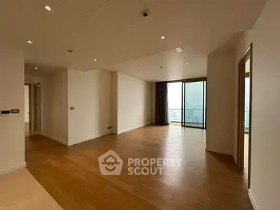 Spacious empty living room with wooden flooring and large windows offering city views.