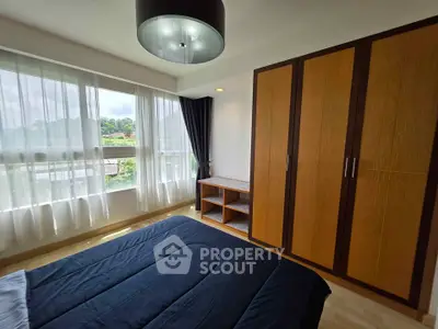 Spacious bedroom with large window and wooden wardrobe, offering natural light and serene views.