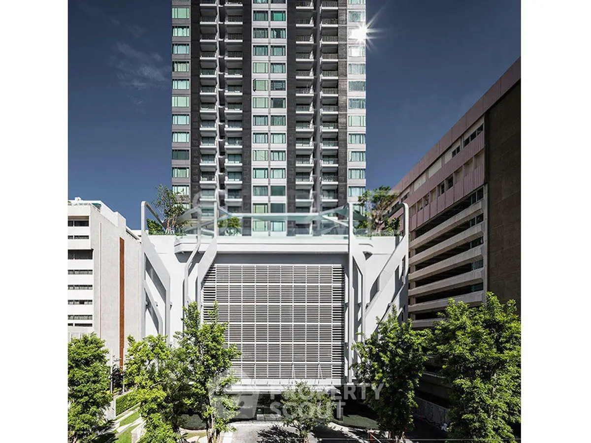 Modern high-rise building with sleek design and lush greenery in urban setting.