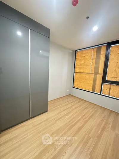 Modern bedroom with sleek wardrobe and large windows, featuring natural light and wooden flooring.