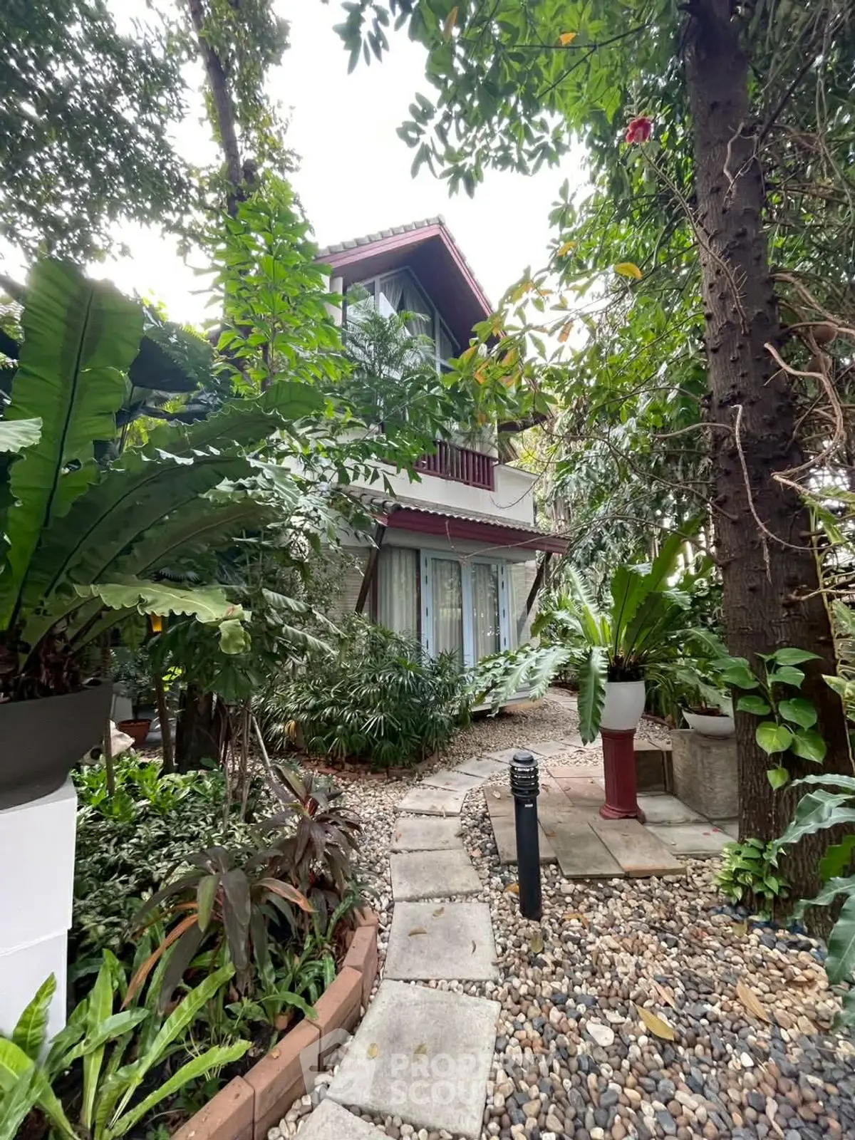 Charming two-story house surrounded by lush greenery and a serene garden path.