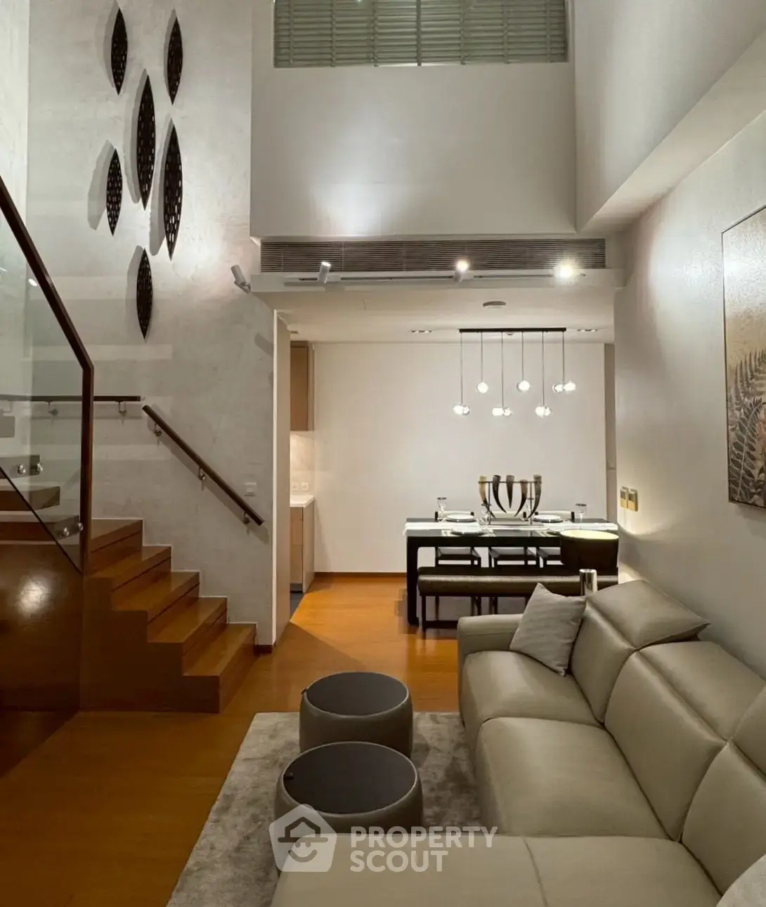Modern living room with elegant staircase and dining area, featuring stylish lighting and contemporary decor.