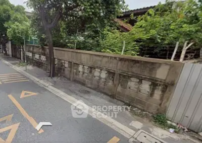 Street view of residential area with concrete wall and lush greenery