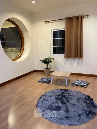 Cozy minimalist room with round window, wooden floor, and stylish decor for a serene living space.