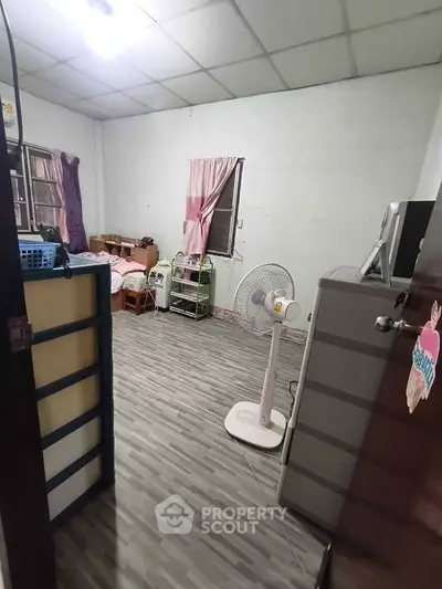 Cozy bedroom with fan, dresser, and bed in a minimalist style, perfect for comfortable living.