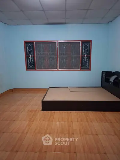 Spacious bedroom with wooden flooring and large window, ideal for customization.