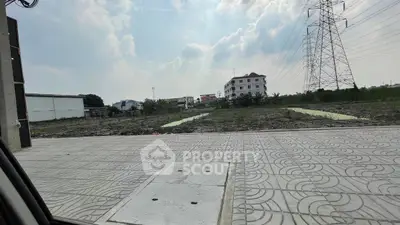 Vacant land plot with paved sidewalk and distant buildings under a cloudy sky.