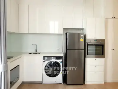 Modern kitchen with sleek white cabinets, stainless steel fridge, oven, and washing machine.