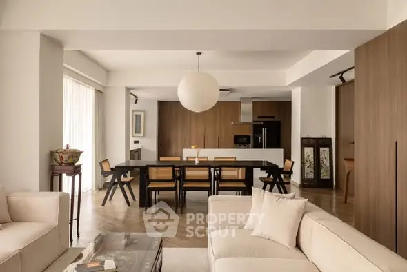 Spacious modern living room with open kitchen and elegant dining area, featuring stylish furniture and warm lighting.