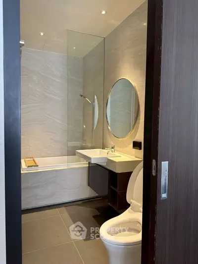 Modern bathroom with sleek design, featuring a round mirror and bathtub.