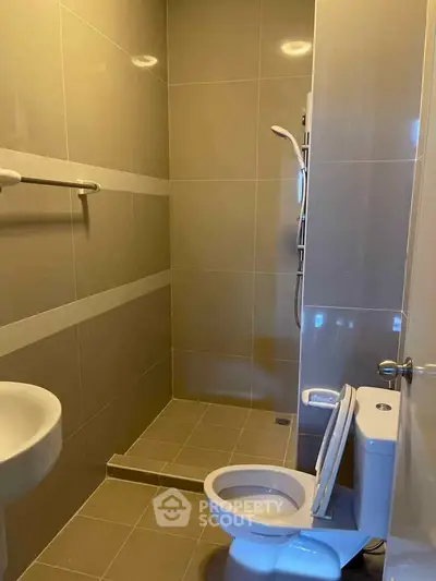Modern bathroom with sleek tiles and compact design, featuring a shower and toilet.