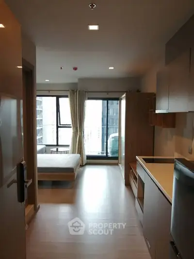 Modern studio apartment with open layout and large windows offering city views.