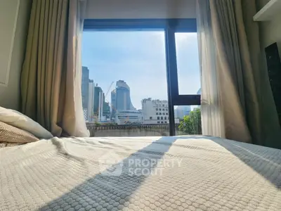 Cozy bedroom with stunning city view through large window, perfect urban retreat.