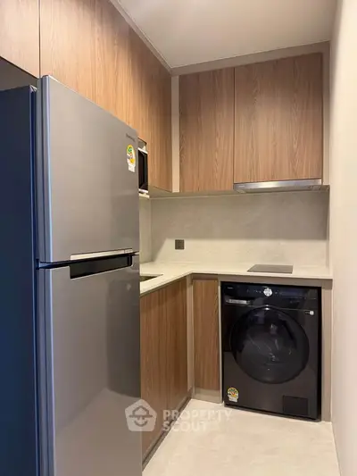 Modern kitchen with sleek appliances and wooden cabinetry, featuring a fridge and washing machine.