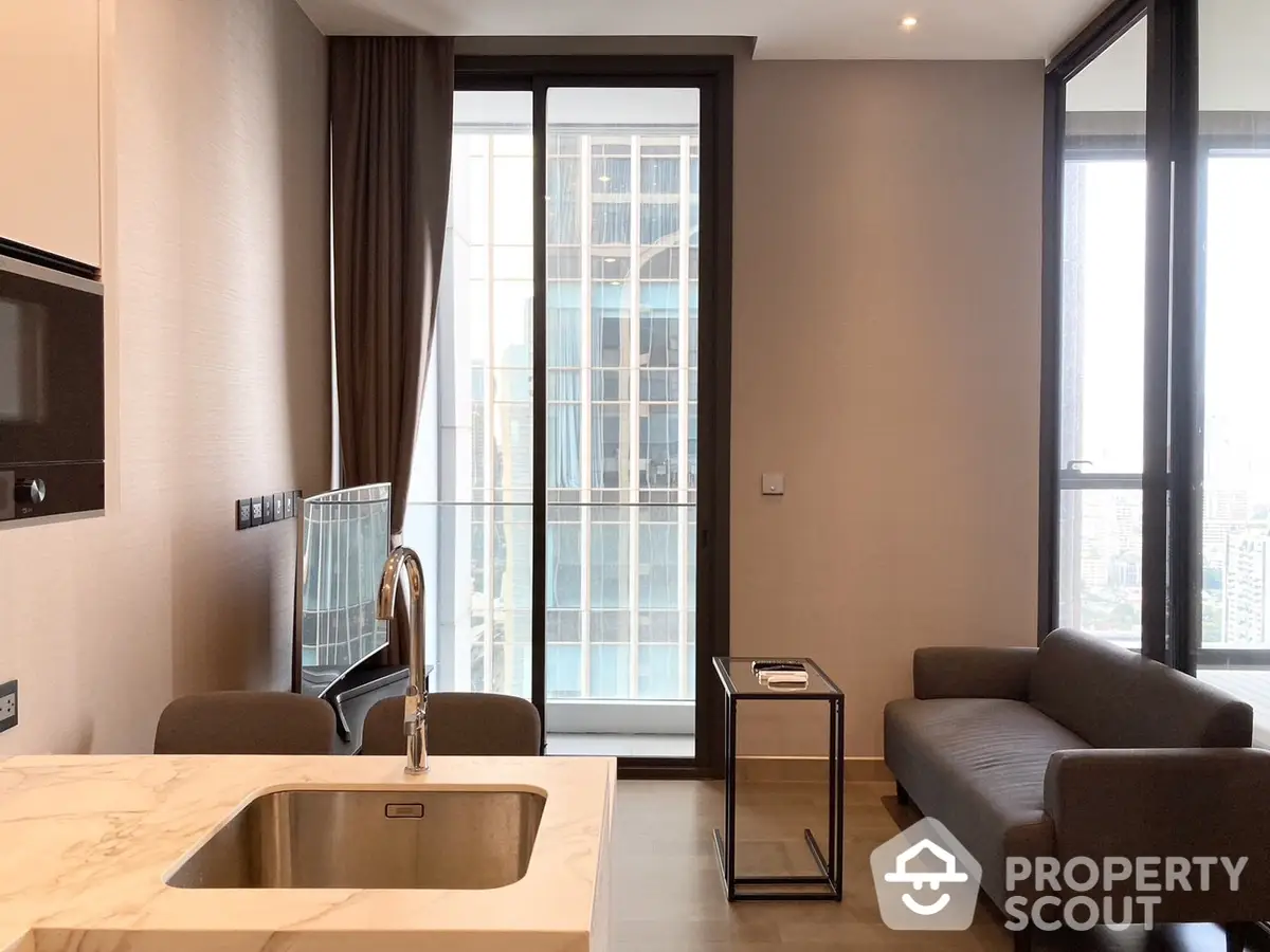 Modern open-plan kitchen with marble countertops and stainless steel sink, seamlessly transitioning to a cozy living area with plush sofas and floor-to-ceiling windows.