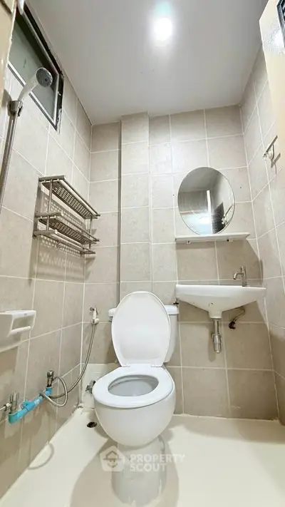 Modern bathroom with tiled walls, round mirror, and compact fixtures.