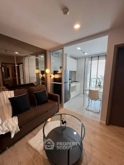 Modern living room with cozy sofa and glass coffee table, adjacent to a sleek kitchen with natural light.