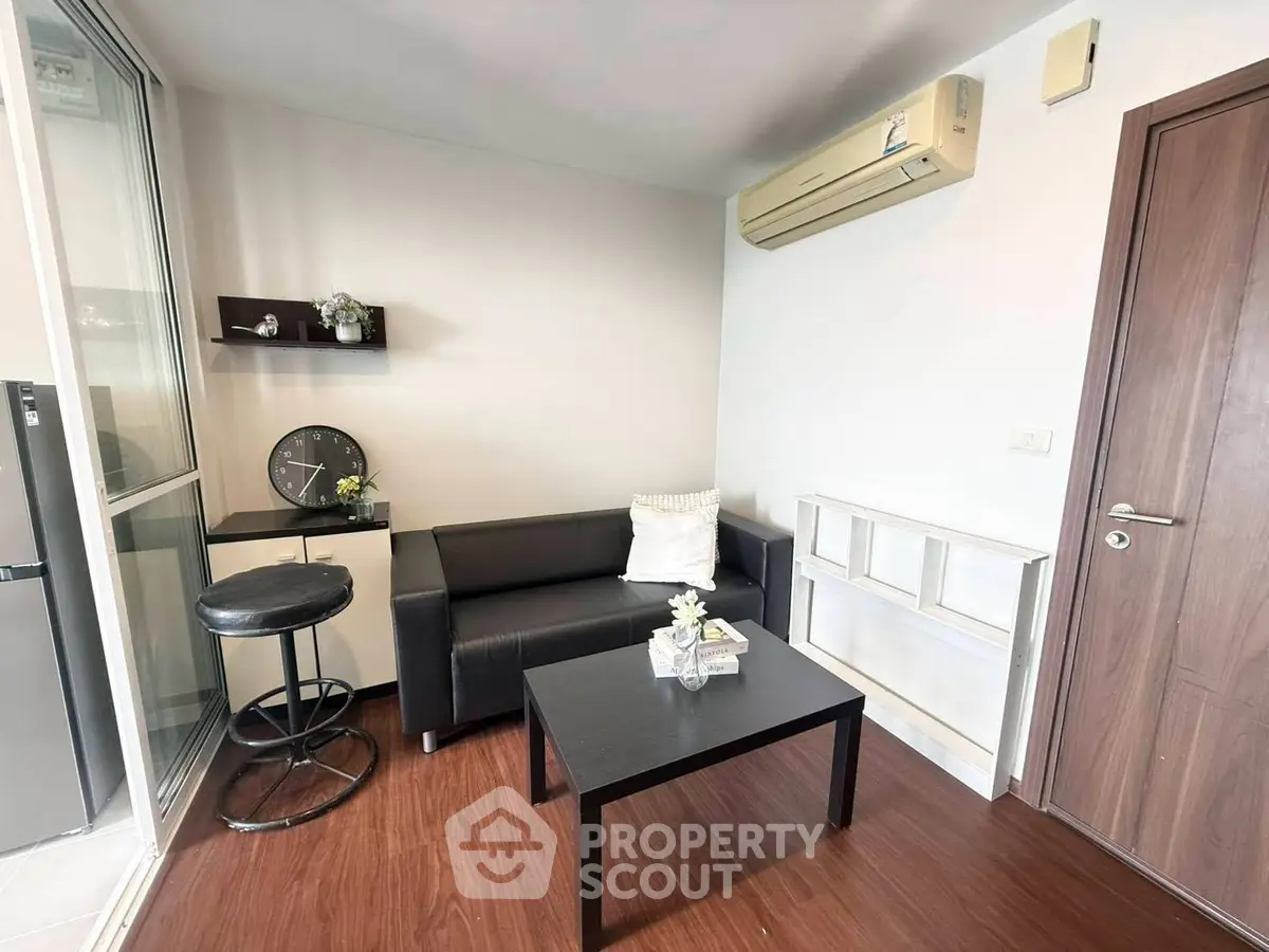 Modern living room with sleek black furniture and wooden flooring, featuring air conditioning and minimalist decor.