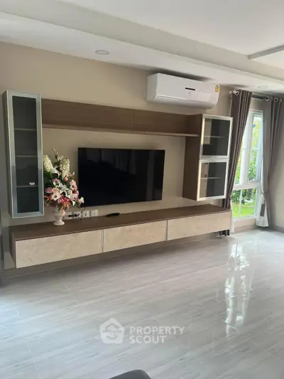Modern living room with sleek TV unit and air conditioning, featuring large windows for natural light.