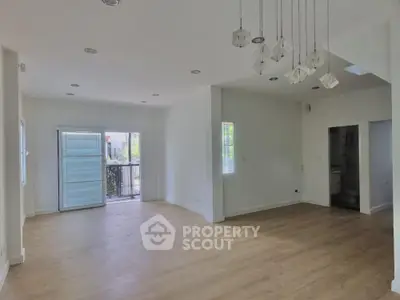 Spacious and bright living room with elegant hardwood floors and modern lighting fixtures, leading to a sunny outdoor area.