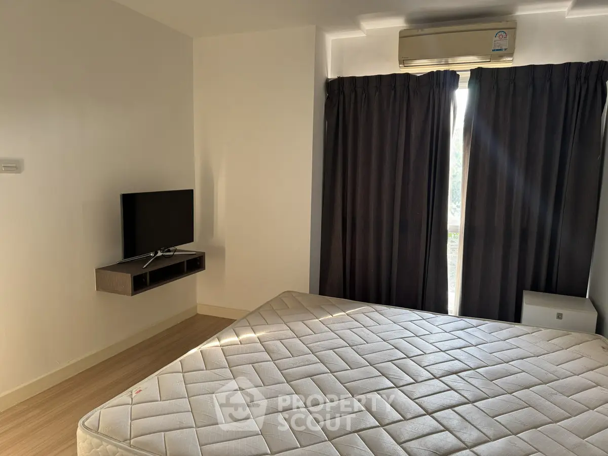 Modern bedroom with natural light, featuring a mounted TV and air conditioning.