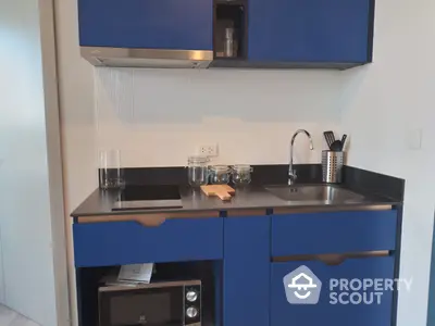 Compact modern kitchenette with striking blue cabinetry, stainless steel sink, and built-in microwave, perfect for urban living.