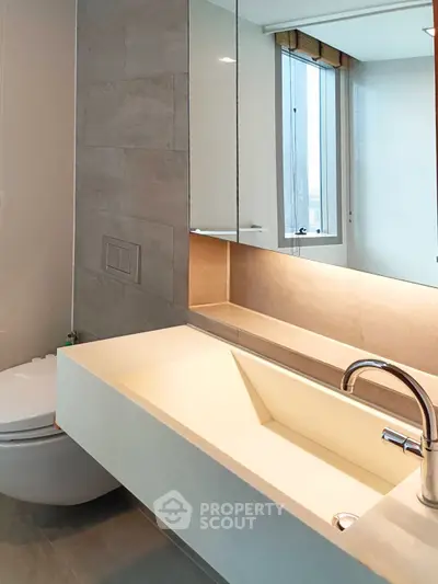 Modern bathroom with sleek sink and wall-mounted toilet, featuring a large mirror and natural light.