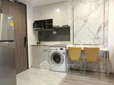 Modern kitchen with washing machine, microwave, and dining area in sleek apartment.