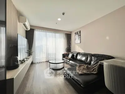 Modern living room with sleek black leather sofa, large TV, and floor-to-ceiling windows offering ample natural light.