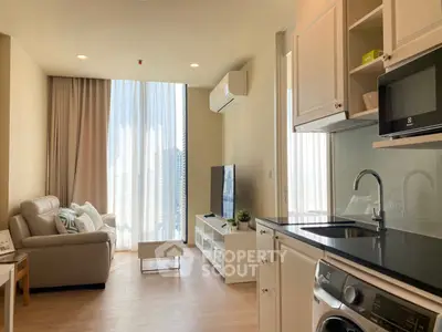 Modern living room with open kitchen, featuring sleek appliances and large windows for natural light.
