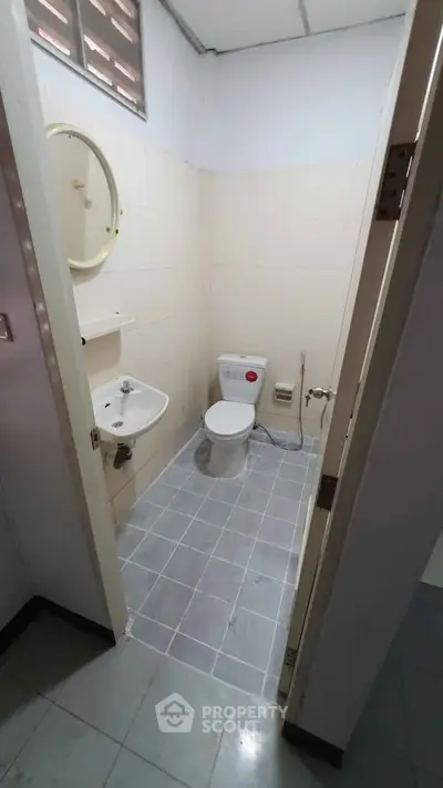 Compact bathroom with toilet, sink, and round mirror in a tiled space.