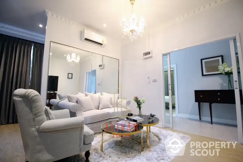 Elegant living room with plush white sofas, chic chandelier, and mirrored wall creating a spacious, luxurious ambiance perfect for upscale living.