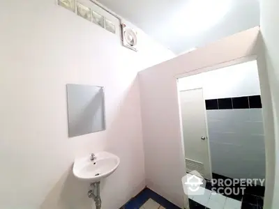 Compact bathroom with white walls, pedestal sink, and wall-mounted mirror, featuring a small window for natural light.