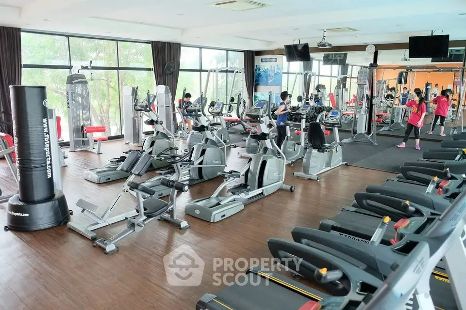 Spacious gym with modern fitness equipment and large windows for natural light.