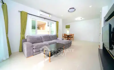 Spacious living room with modern gray sofa and dining area, featuring bright natural light and stylish decor.