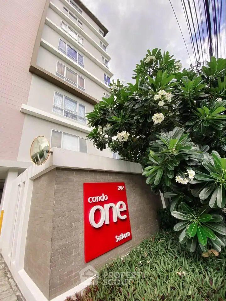 Modern condo building exterior with lush greenery and prominent signage.