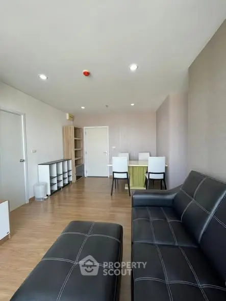 Modern living room with sleek black leather sofa and dining area, featuring wooden flooring and ample natural light.