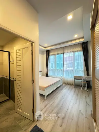 Spacious bedroom with large windows and modern decor, featuring an ensuite bathroom and stylish flooring.