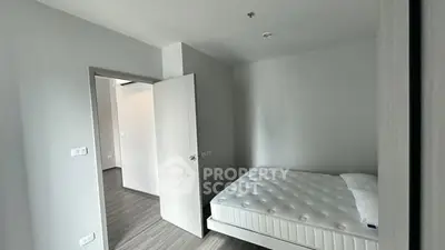 Modern minimalist bedroom with white walls and bed, open door leading to hallway.