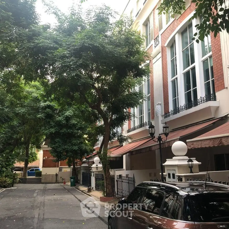 Charming townhouse exterior with lush trees and parked car in a serene neighborhood setting.